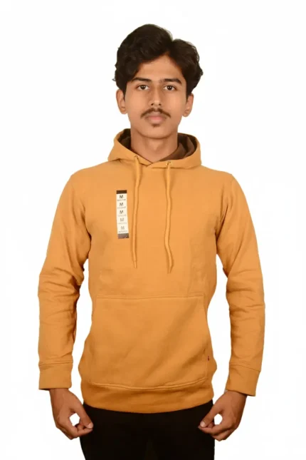 A person wearing a mustard-colored hoodie with a front pocket, standing against a plain white background.
