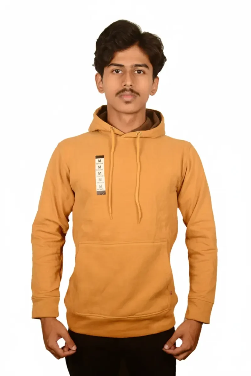 A person wearing a mustard-colored hoodie with a front pocket, standing against a plain white background.