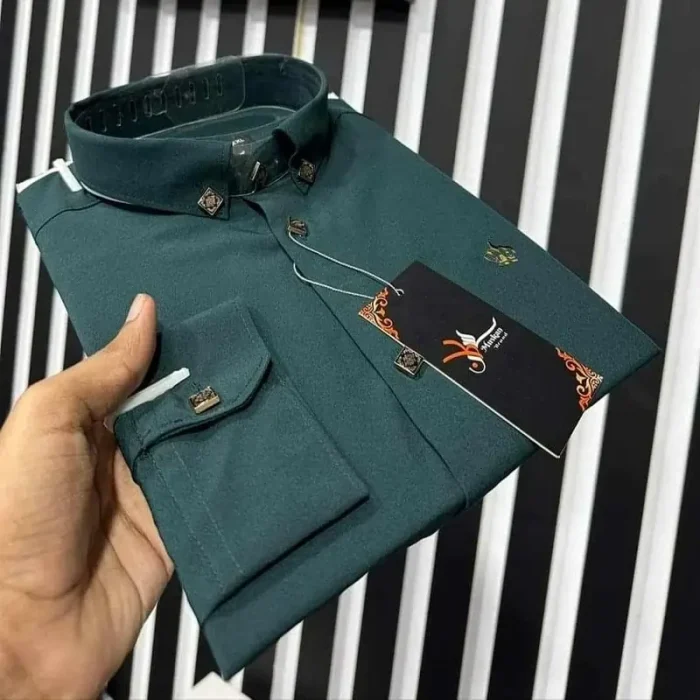 A folded teal shirt with tags on a striped background, held by a person's hand.