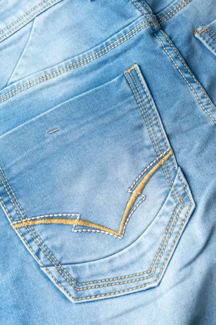 Close-up of a light blue denim pocket with yellow stitching.