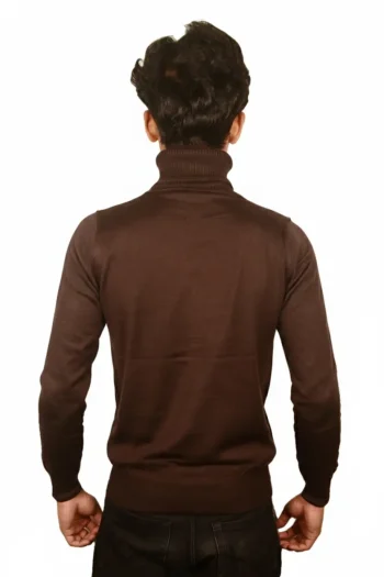 A person stands with their back to the camera, wearing a brown turtleneck sweater and black pants against a white background.
